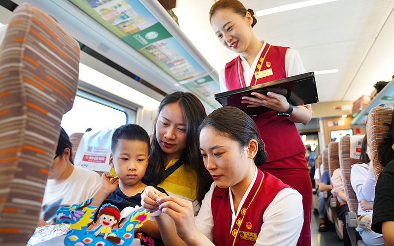 6月22日，G305次列車乘務(wù)人員幫助小旅客制作龍舟手工。劉超攝